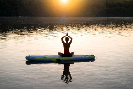 Woman meditating and practicing yoga during sunrise on a paddleboardの写真素材