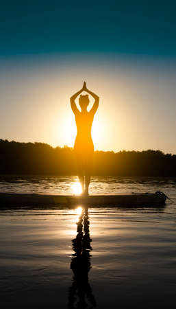 Woman meditating and practicing yoga during sunrise on a paddleboardの写真素材