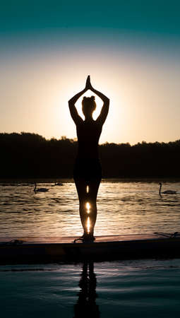 Woman meditating and practicing yoga during sunrise on a paddleboardの写真素材
