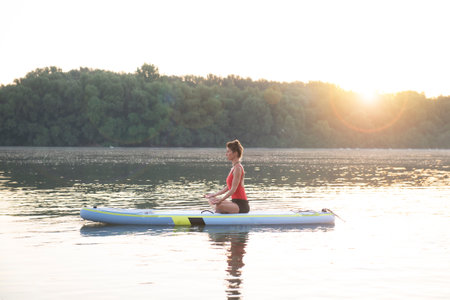 Woman meditating and practicing yoga during sunrise on a paddleboardの写真素材