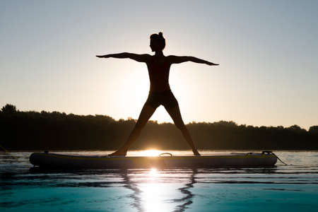 Woman meditating and practicing yoga during sunrise on a paddleboardの写真素材