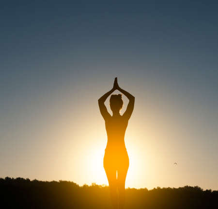 Woman meditating and practicing yoga during sunrise on a paddleboardの写真素材
