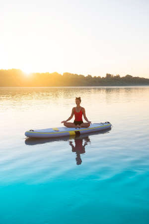 Woman meditating and practicing yoga during sunrise on a paddleboardの写真素材