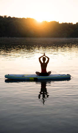 Woman meditating and practicing yoga during sunrise on a paddleboardの写真素材