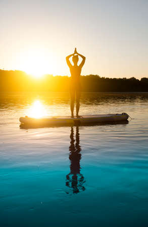 Woman meditating and practicing yoga during sunrise on a paddleboardの写真素材
