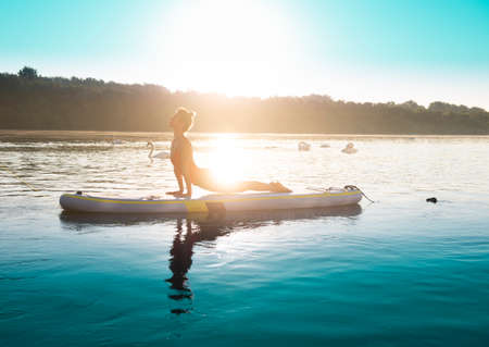 Woman meditating and practicing yoga during sunrise on a paddleboardの写真素材