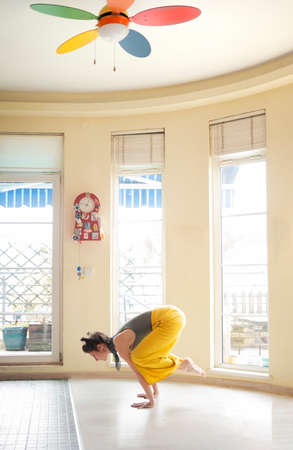 Beautiful woman relaxing in her home doing yoga and standing in a crow poseの写真素材