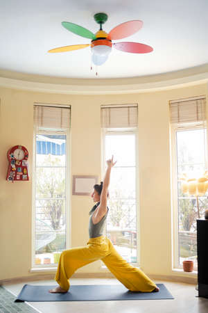 Young woman standing in a Warrior I pose during her yoga lesson at homeの写真素材