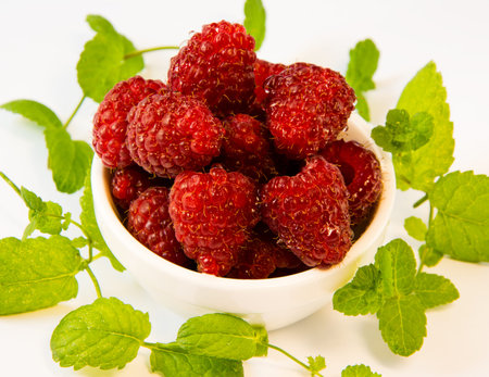 raspberries  in a white plate with mint on a white table