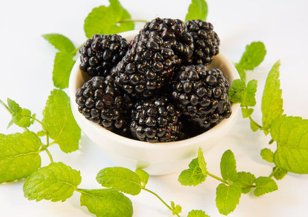 blackberries  in a white plate with mint on a white table