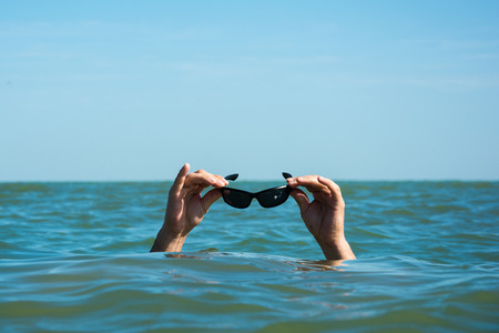 The man in the sea is holding sunglasses above the waterの写真素材