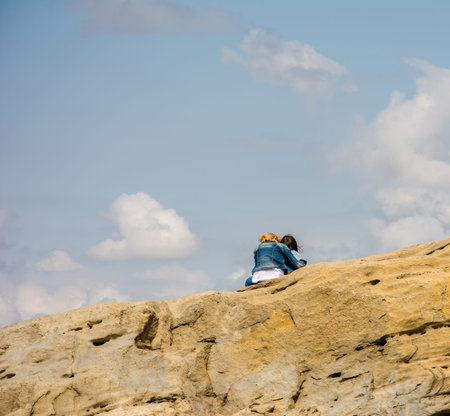 Mother and daughter sit on top of the mountain against the blue sky with white clouds