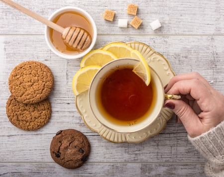 woman drinking tea with lemon . cookies, sugar , honey and  lying on a white wooden table closeupの写真素材