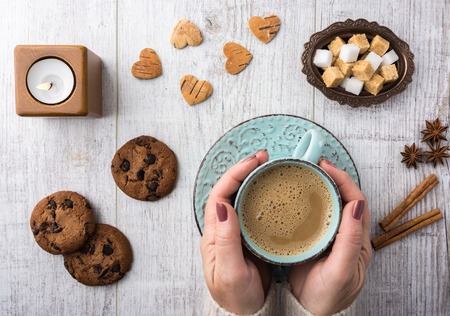 Women drinking coffee with milk. Cookies, sugar, cinnamon, star anise and candle lying on a white wooden table top viewの写真素材