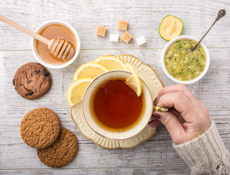 woman drinking tea with lemon . cookies, sugar , honey, feijoa and jam feijoa  lying on a white wooden table top viewの写真素材