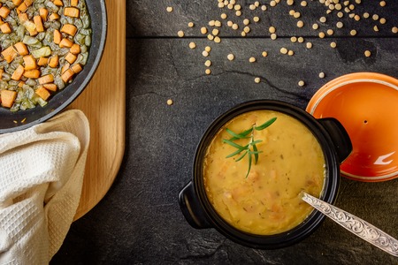 pea soup with carrots and onions in a black pot on a dark table top viewの写真素材
