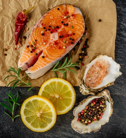 Delicious salmon steak , rich in omega 3 oil, with aromatic herbs and spices with a lemon, tomato, garlic on black background. Healthy and diet food. Top view.の写真素材
