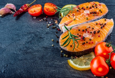 Delicious salmon steak , rich in omega 3 oil, with aromatic herbs and spices with a lemon, tomato, garlic on black background. Healthy and diet food.の写真素材