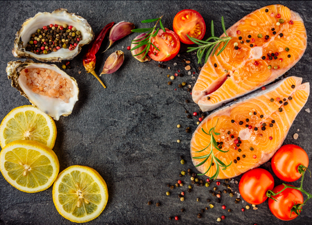 Delicious salmon steak , rich in omega 3 oil, with aromatic herbs and spices with a lemon, tomato, garlic on black background. Healthy and diet food. Top view.の写真素材