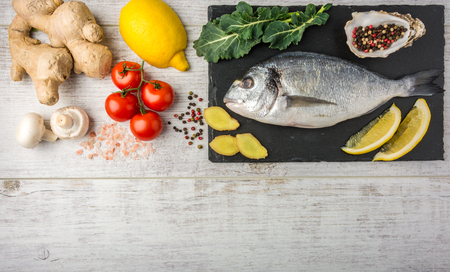 Useful dorado fish, rich in protein, vitamins, Omega 3 with vegetables, lemon and ginger, prepared for cooking on a white wooden table. Top viewの写真素材