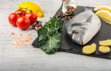 Useful dorado fish, rich in protein, vitamins, Omega 3 with vegetables, lemon and ginger, prepared for cooking on a white wooden table.の写真素材