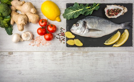 Useful dorado fish, rich in protein, vitamins, Omega 3 with vegetables, lemon and ginger, prepared for cooking on a white wooden table. Top viewの写真素材