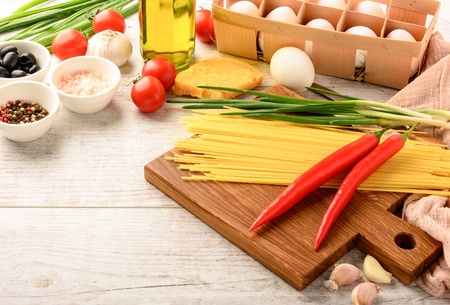 Ingredients for cooking healthy Italian food and cutting board on a white wooden table with space for an object in a home kitchenの写真素材