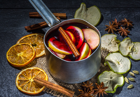 Small stewpot with mulled wine and cinnamon sticks, dry slice of oranges and apple, star anise on a dark tableの写真素材