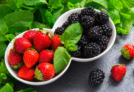 strawberries and blackberries in a white ceramic cups on a dark tableの写真素材