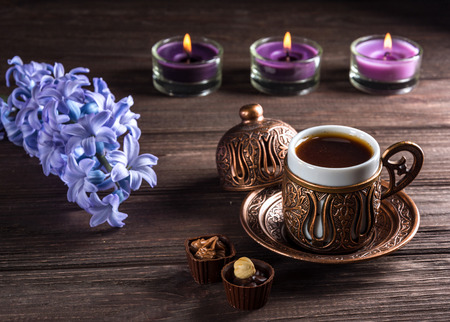 Cup of black coffee, candles and flowers on a wooden background. Dark key.の写真素材