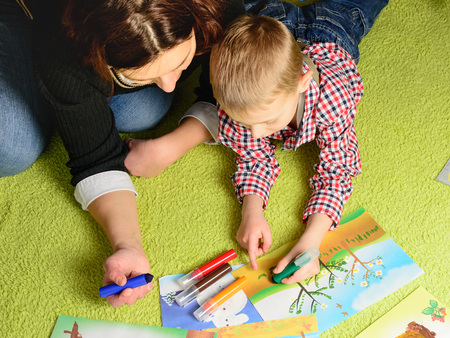 the child together with mother draws a picture lying on a green carpetの写真素材