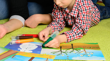 the child together with mother draws a picture lying on a green carpetの写真素材