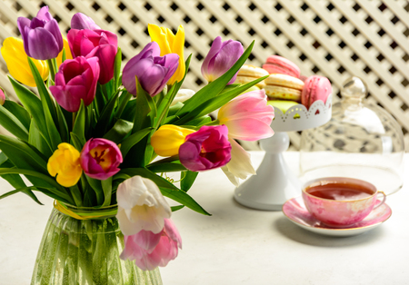 Beautiful festive bouquet of tulips, cakes and cup of tea on white background.の写真素材