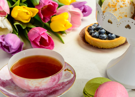 Beautiful festive bouquet of tulips, cakes and cup of tea on white background.の写真素材