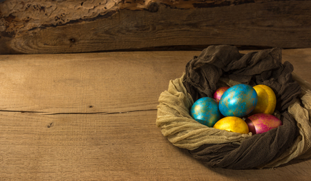 Multi-colored Easter eggs in a nest of soft scarf on a natural wooden background. Copy space.の写真素材