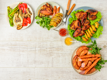 Dinner table with variety food, fried chicken wings, sausages, grilled vegetables in a pan, salad and  lager beer on wooden table. Top view. Copy space. Indoor food Concept.の写真素材