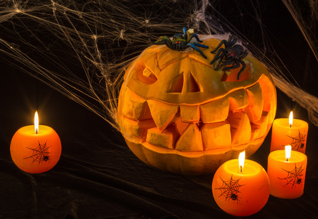 There are the horrible pumpkin and burning orange candles on a black table.Everything prepares for the holiday of Halloweenの写真素材