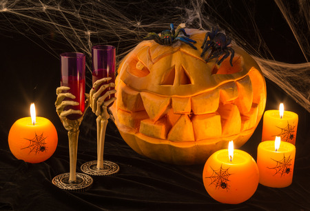There are the horrible pumpkin and burning orange candles on a black table.Everything prepares for the holiday of Halloweenの写真素材