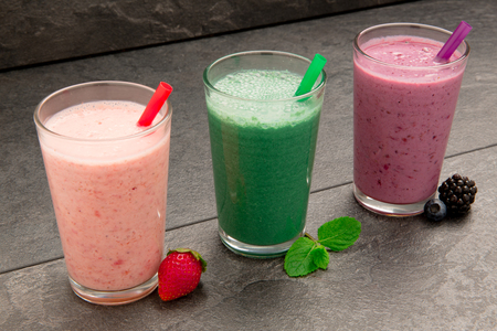 Fresh strawberry, spinach, blueberry, blackberry and mint smoothie with straw on black backgroundの写真素材