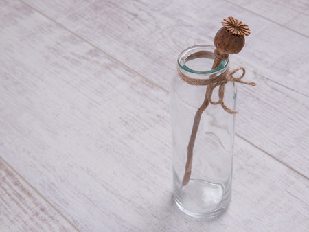 Brown poppy stick in the glass bottle on the white table decorated with sackcloth bowの写真素材