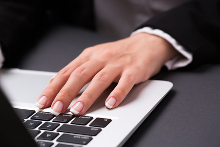 Young office woman in the black suite and with manicure is holding hand on the laptop keyboardのeditorial素材