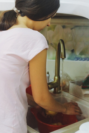 young woman washes potatoes in a sink in the kitchen.の写真素材
