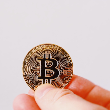 A golden bitcoin on a sheet of white paper is holding a finger. Bitcoin is a crypto currency. Bitocoin isolated on white background.の写真素材