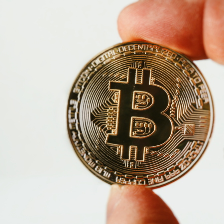 A golden bitcoin on a sheet of white paper is holding a finger. Bitcoin is a crypto currency. Bitocoin isolated on white background.の写真素材