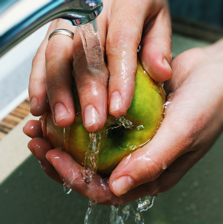 Women Hands Wash Apple under Jet of Water in the sink. The apple is juicy, clean. Apple - red-yellow. Water splash.の写真素材