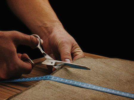 Men Hands Cut Fabric on a dark background. Scissors in male hands. Tape measure. Measure the fabric.