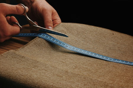 Men Hands Cut Fabric on a dark background. Scissors in male hands. Tape measure. Measure the fabric.の写真素材
