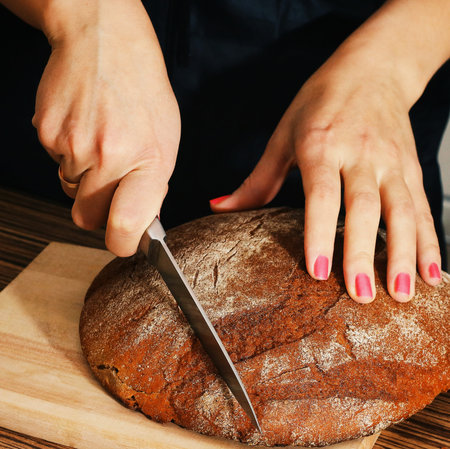 Female hands Cutting dark Bread on a wooden board.