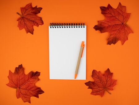 Autumn composition with blank notepad, pen and autumn leaves on orange background. workplace. flatlay. top view. copyspace.の写真素材