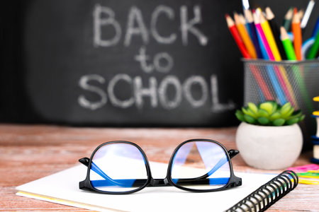 Glasses, school supplies and a blackboard in the background with the words "Back to school". close-up. selective focus.の写真素材